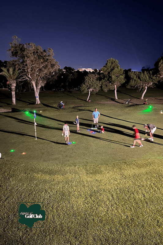Nighttime family golf activity with illuminated golf balls and equipment.